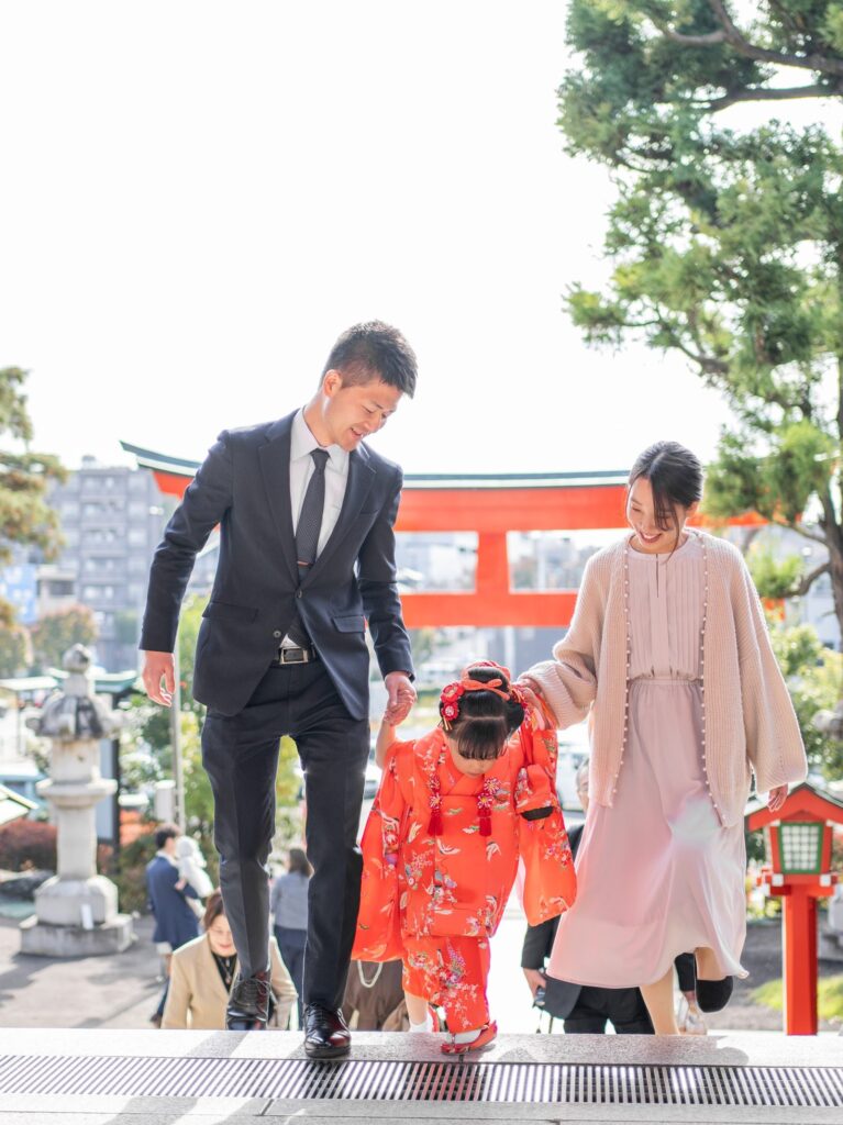 神社の鳥居の前を歩く七五三の女の子と家族